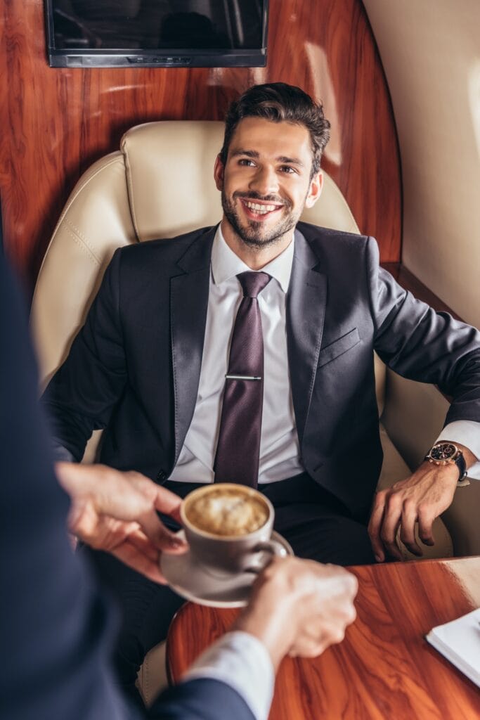 cropped view of flight attendant giving cup of coffee to handsome businessman in suit in private
